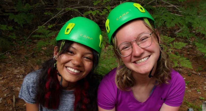 Two young people wearing green helmets smile at the camera. 